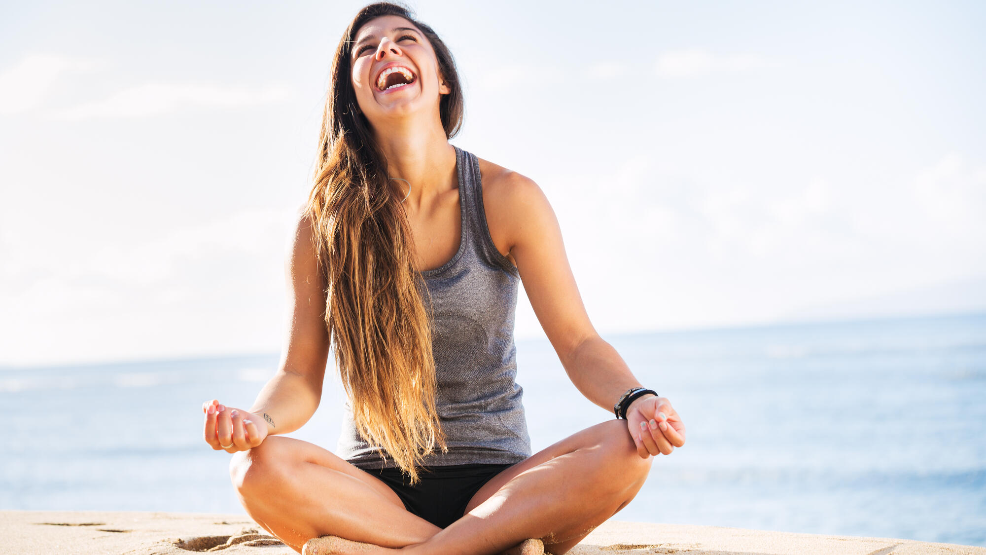 Smiling woman sitting on the beach in a yoga position 